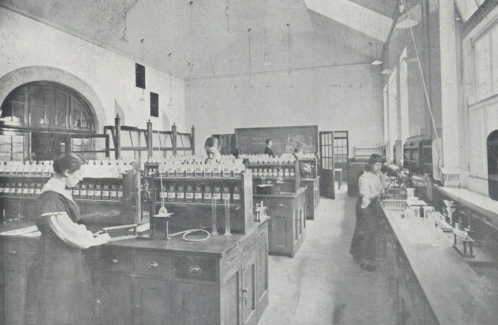 Black and white photograph. Men and women pictured working in a chemistry laboratory.